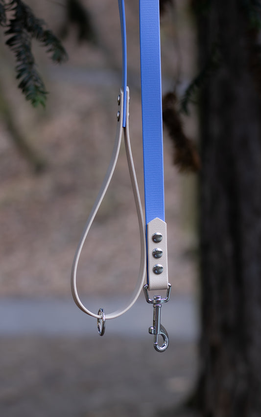 Na fotce je elegantní voděodolné vodítko s ručkou v kombinaci modré a béžové. Toto lehce omyvatelné biothanové vodítko je děláno ručně na míru a skvěle se hodí na procházky se všemi plemeny psů.